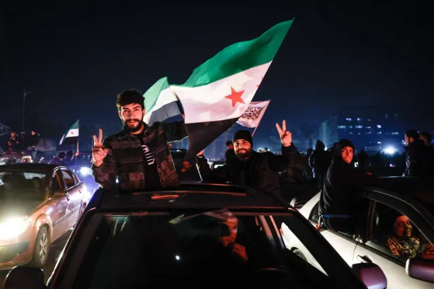 سوريون يرفعون علامة النصر ويلوحون بأعلام سوريا احتفالاً بسقوط نظام الرئيس بشار الأسد في ساحة الأمويين بدمشق 11 ديسمبر 2024 (إ.ب.أ)