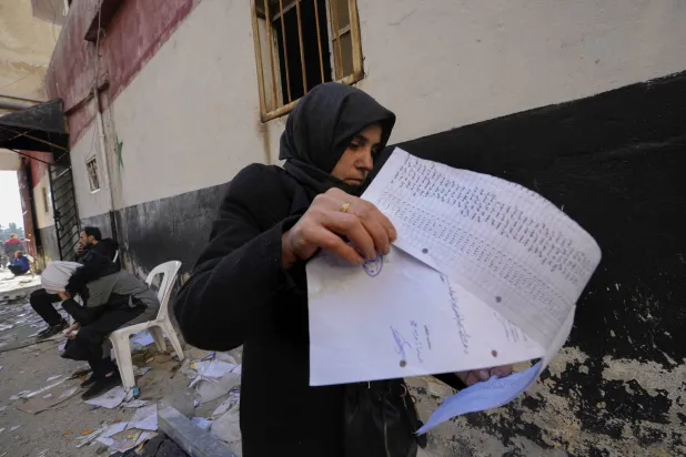 امرأة تتصفح قائمة أسماء وُجدت على الأرض في سجن صيدنايا العسكري شمال دمشق 9 ديسمبر (أ.ب)