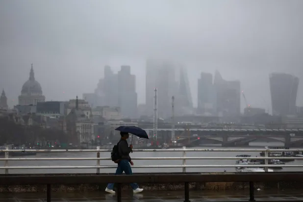 A pedestrian walks across Waterloo Bridge in the drizzle with the buildings of the City of London financial district behind, in London on December 13, 2024. (Photo by HENRY NICHOLLS / AFP)