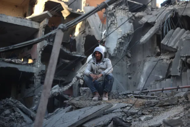 فلسطيني فوق أنقاض مبنى دمره القصف الإسرائيلي في مخيم النصيرات بغزة الجمعة (أ.ف.ب)