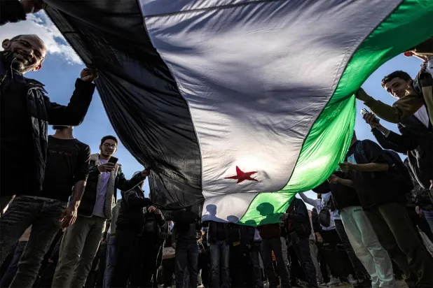 يلوح الناس بعلم الثورة السورية بعد الإطاحة ببشار الأسد (أ.ف.ب)