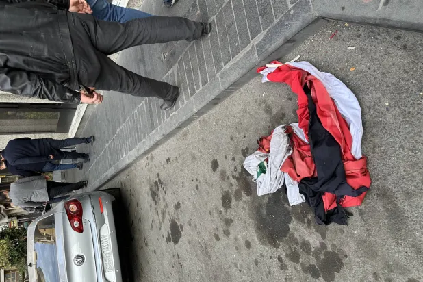 سوريون يمرون بعلم سوري قديم وممزق في أحد شوارع دمشق (الشرق الأوسط)