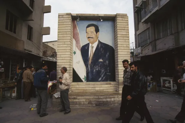 عراقيون يسيرون أمام جدارية ضخمة لصدام حسين في بغداد عام 1991 (غيتي)