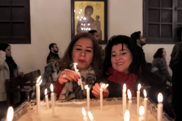 المصلون يشعلون الشموع خلال قداس صباح عيد الميلاد في كاتدرائية القديس جاورجيوس للروم الأرثوذكس بمدينة اللاذقية (أ.ف.ب)