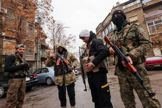 مقاتلون من الحرس السوري الحاكم بجوار المباني المحيطة بأحد مراكز المخابرات والسجون بعد الإطاحة بالرئيس السوري السابق بشار الأسد في دمشق يوم 29 ديسمبر 2024 (رويترز)