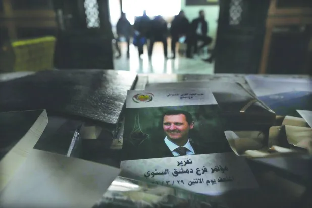 صورة الرئيس السوري المخلوع بشار الأسد على غلاف تقرير فوق مكتب بمقر «حزب البعث» حيث ينتظر جنود سابقون تسجيل أسمائهم في «عملية المصالحة» في دمشق الاثنين (أ.ب)