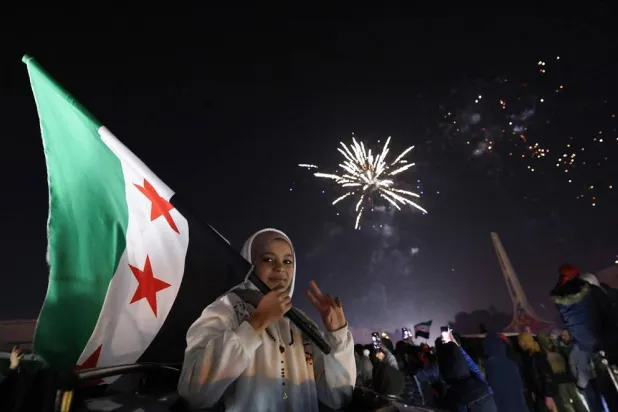 A young woman holds the Flag of Syria as people celebrate the New Year near Umayyad Square in Damascus, Syria, on January 1, 2025. (AFP)