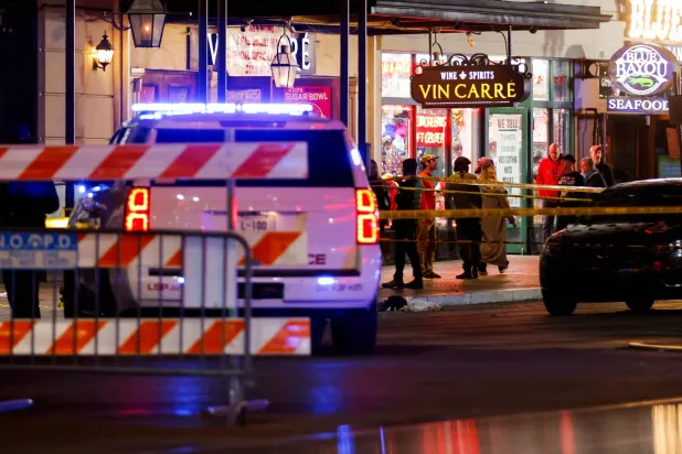 تقف سيارات إنفاذ القانون والأشخاص بالقرب من مكان الحادث حيث اصطدمت سيارة بحشد من الناس خلال احتفالات رأس السنة الجديدة في نيو أورليانز بولاية لويزيانا (رويترز)