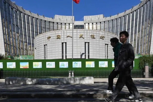 صينيان يمران أمام مقر البنك المركزي بالعاصمة بكين (رويترز)