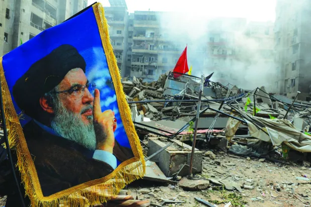 صورة لحسن نصر الله أمام أنقاض مبنى دمّره الطيران الإسرائيلي في الضاحية الجنوبية لبيروت (د.ب.أ)