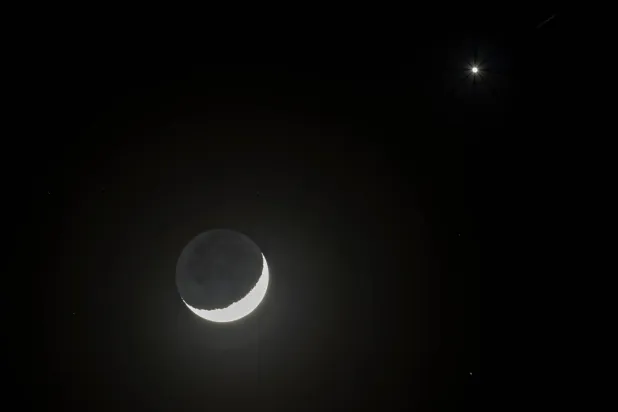 يتم رصد القمر وكوكب الزهرة في السماء فوق المجر (إ.ب.أ)