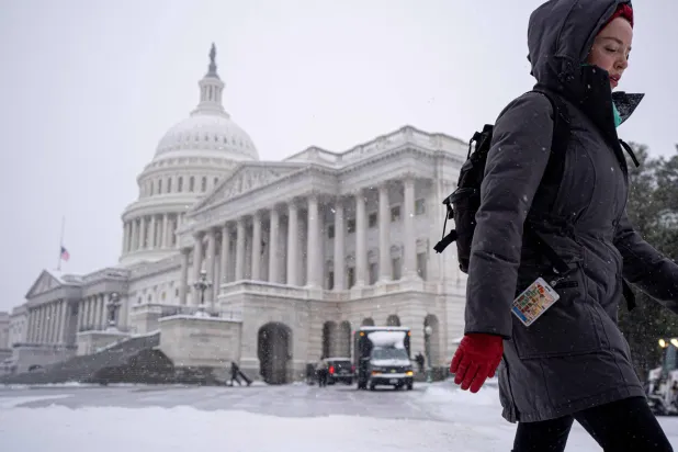 مبنى الكابيتول يظهر أثناء سير امرأة عبر عاصفة شتوية في العاصمة الأميركية (أ.ف.ب)