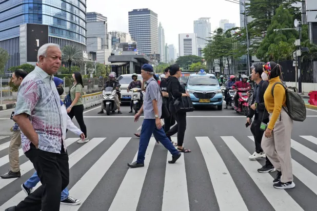 مشاة يعبرون طريقاً في الحي المالي وسط العاصمة الإندونيسية جاكرتا (أ.ب)