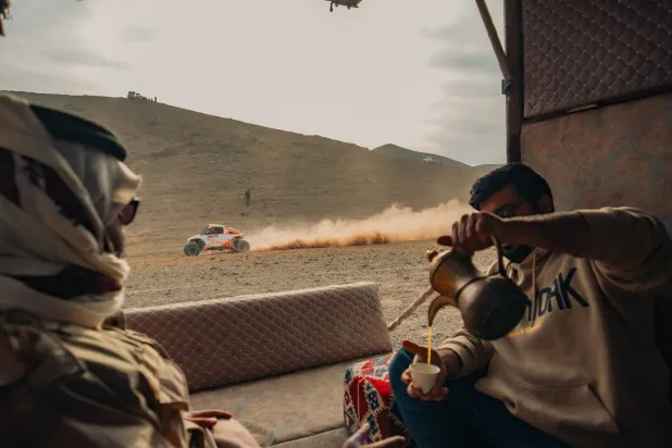 مواطنان يتناولان القهوة السعودية فيما يمر بجانبهم أحد المتسابقين (الشرق الأوسط) 