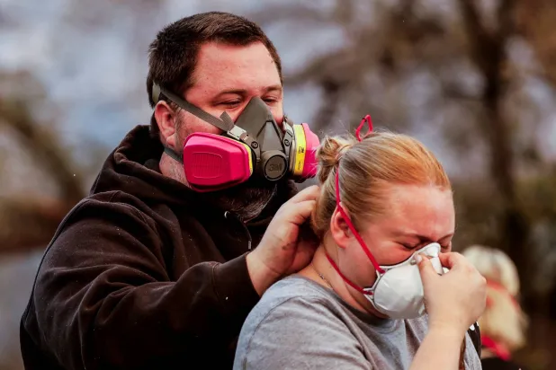 براندون رود يساعد زوجته على ارتداء قناع وجه خلال تفقُّدهم الدمار الذي لحق منزلهم جراء حرائق لوس أنجليس (رويترز)