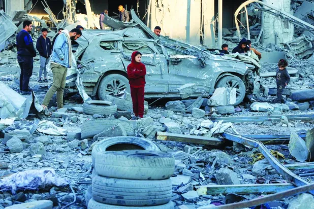 Filistinliler, İsrail'in dün Gazze Şehri'ne düzenlediği bombalamanın ardından çöken bir binanın enkazının ortasında, tahrip olmuş arabanın önünde duruyor (AFP)