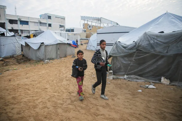 فتيات فلسطينيات يمررن أمام خيام تؤوي فلسطينيين نازحين في مخيم قبل وقف إطلاق النار المقرر أن يدخل حيز التنفيذ يوم الأحد في مدينة غزة (رويترز)