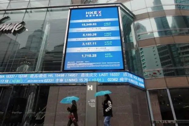 مارة يمشون أمام شاشات تعرض مؤشر بورصة هونغ كونغ وأسعار الأسهم (رويترز)