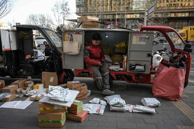 A delivery worker sits on a delivery vehicle along a street in Beijing on January 17, 2025. (Photo by Jade GAO / AFP)