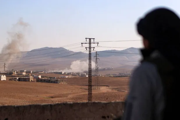 مقاتل من فصيل مدعوم من تركيا يشاهد عموداً من الدخان يتصاعد خلال الاشتباكات في منبج (أ.ف.ب)