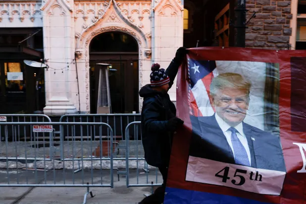رجل يحمل لافتة عليها صورة ترمب بينما يتجمع أنصاره خارج ساحة «كابيتال وان» تحضيراً للاحتفال بتنصيبه (رويترز)