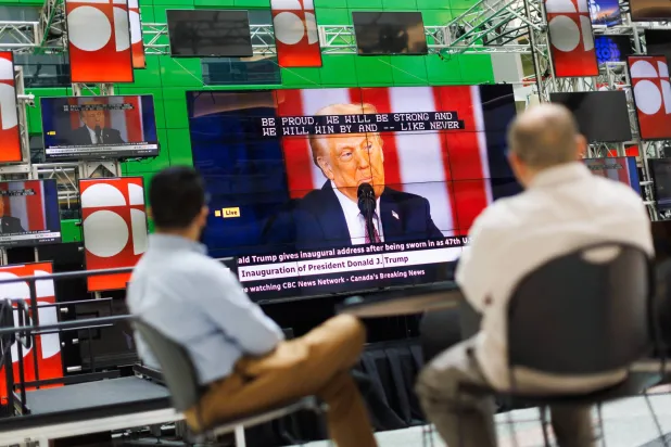 شخصان يتابعان حفل تنصيب ترمب على الهواء مباشرة خلال شاشة في بهو مبنى هيئة الإذاعة الكندية في تورونتو (د.ب.أ)