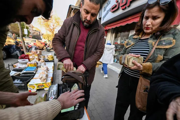 صراف يعمل مع زبائن في أحد شوارع دمشق (أ.ف.ب)