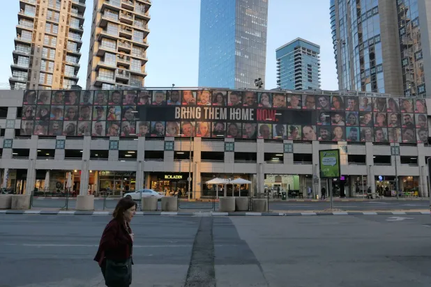 امرأة تمر أمام لوحة إعلانية كبيرة تحمل صور الرهائن الإسرائيليين المحتجزين لدى «حماس» في قطاع غزة... تل أبيب 21 يناير 2025 (إ.ب.أ)