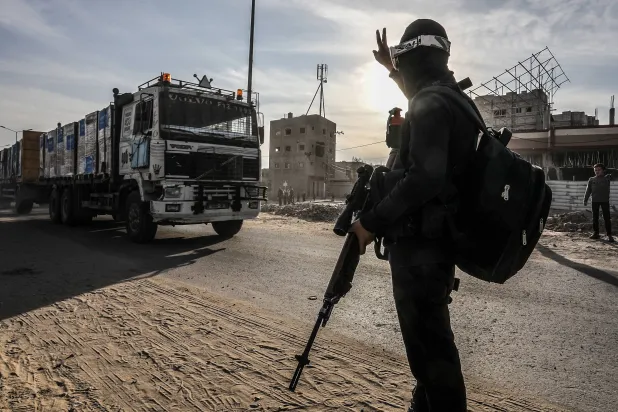 مقاتل فلسطيني يرفع علامة النصر لدى دخول شاحنات تحمل مساعدات على طريق صلاح الدين شرق خان يونس 19 يناير 2025 (د.ب.أ)