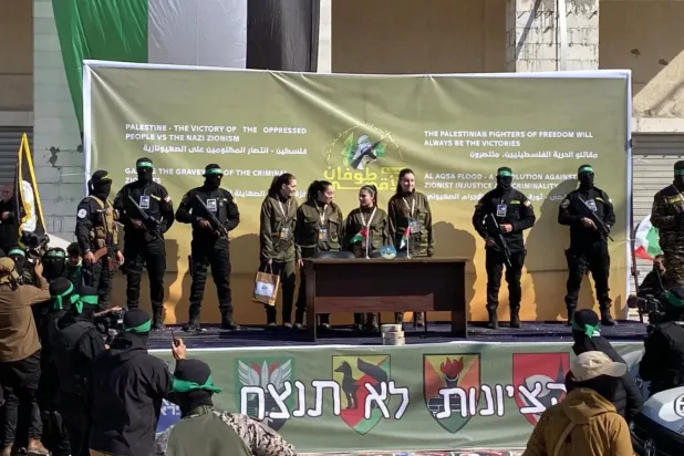 Dün dört İsrailli kadın askeri Kızıl Haç ekibine teslim etmeden önce sahnede onlara eşlik den Hamas üyeleri (DPA)