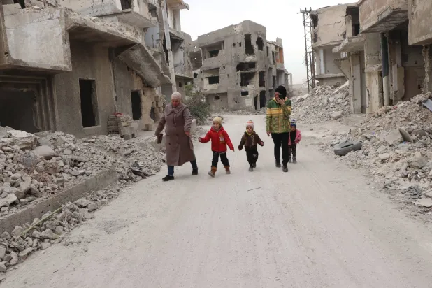 أسرة سورية تمر بين أنقاض المنازل في أطراف شمال شرقي دمشق (الشرق الأوسط)