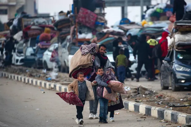 رجل فلسطيني وأطفاله يحملون أمتعتهم بينما تصطف المركبات على طول طريق صلاح الدين في النصيرات بالقرب من ممر نتساريم أثناء انتظارهم العبور إلى الجزء الشمالي من قطاع غزة يوم 27 يناير 2025 (أ.ف.ب)