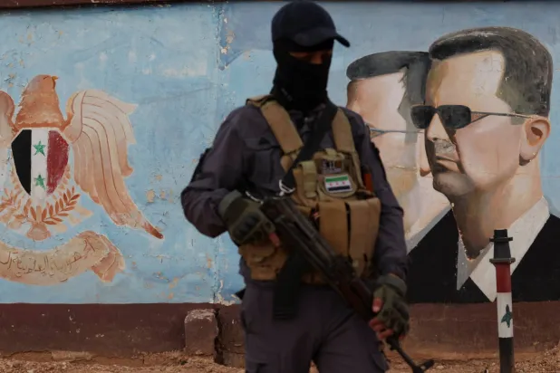 أحد عناصر الفصائل المسلحة يقف بالقرب من صورة للرئيس السوري بشار الأسد في مقر الفرقة الرابعة في دمشق بسوريا في 23 يناير 2025 (رويترز)