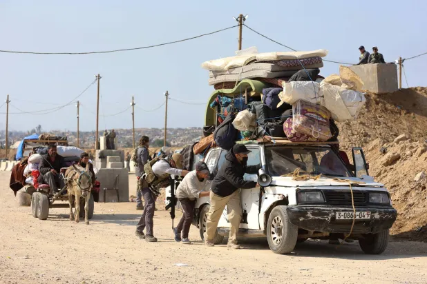 رجال يساعدون في دفع مركبة محملة بينما يعبر فلسطينيون نازحون نقطة تفتيش يديرها الأمن الأميركي والمصري بممر نتساريم في طريقهم من الجنوب إلى الأجزاء الشمالية بقطاع غزة (أ.ف.ب)