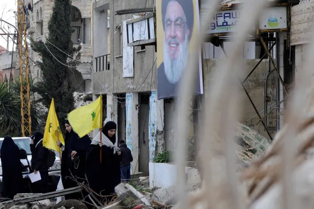 Residents of the southern Lebanese village of Khiam wave Hezbollah flags as they walk beneath a portrait of slain Hezbollah leader Hassan Nasrallah on their return to their village on January 27, 2025. (Photo by Rabih DAHER / AFP)