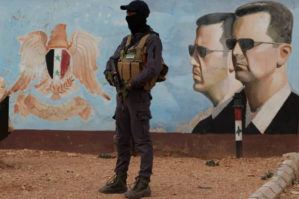 أحد أعضاء جماعة «هيئة تحرير الشام» يقف حارساً بالقرب من صورة للرئيس المخلوع بشار الأسد في مقر الفرقة الرابعة بدمشق (رويترز)