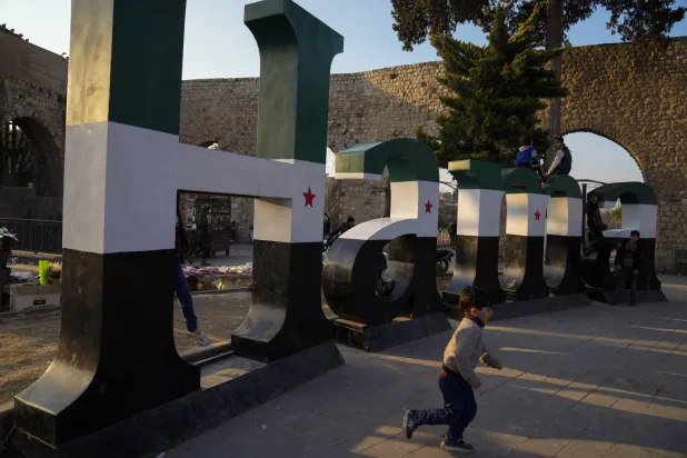 أطفال يلهون قرب نموذج يحمل اسم مدينة حماة مطلي بألوان العلم السوري الجديد في الساحة الرئيسية للمدينة 26 يناير الماضي (أ.ب)