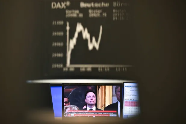 منحنى «داكس» يظهر تحركات صعودية وهبوطية في غرفة التداول ببورصة فرانكفورت بينما يمكن رؤية الملياردير التكنولوجي إيلون ماسك على الشاشة (د.ب.أ)