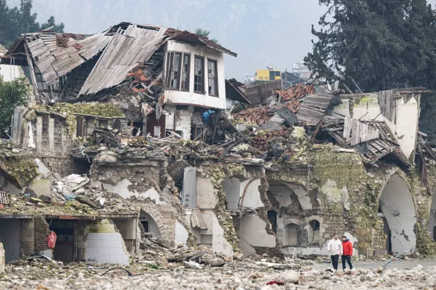 رجلان يسيران أمام منازل دمرها الزلزال في محافظة هاتاي التركية (د.ب.أ)