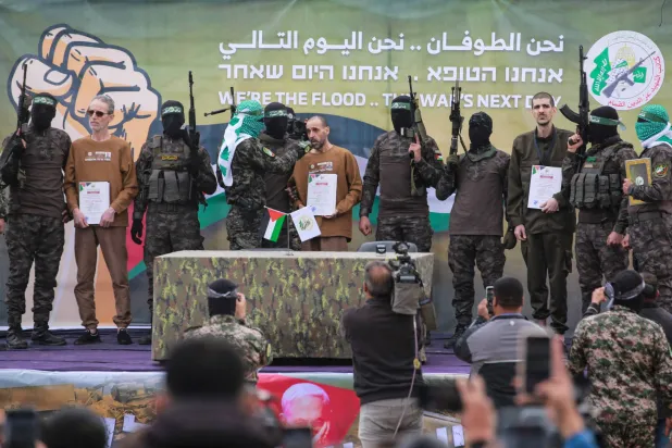 الأسرى الثلاثة على منصة التسليم وسط مقاتلي «القسام» (أ.ف.ب)