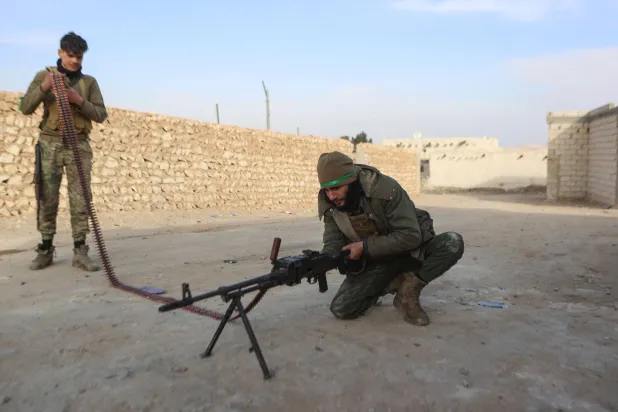 مقاتلان من الفصائل السورية المدعومة من تركيا المشاركة في العمليات شرق حلب في أثناء تجهيز سلاح آلي (أ.ف.ب) 