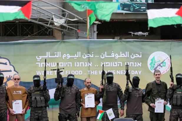 المحتجزون الإسرائيليون الثلاثة بين مقاتلين من «حماس» قبيل تسليمهم للصليب الأحمر بدير البلح السبت (رويترز)