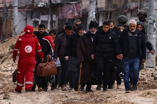 جنود إسرائيليون يراقبون فلسطينيين وهم يغادرون منازلهم بحثاً عن الأمان أثناء مداهمة الجيش لمخيم نور شمس للاجئين بالقرب من طولكرم في الضفة الغربية الاثنين (وكالة الصحافة الفرنسية)