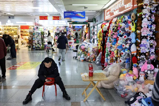 شخص ينظر إلى هاتف ذكي أثناء الجلوس على كرسي في سوق للتجارة الدولية بمقاطعة تشجيانغ - الصين (رويترز)