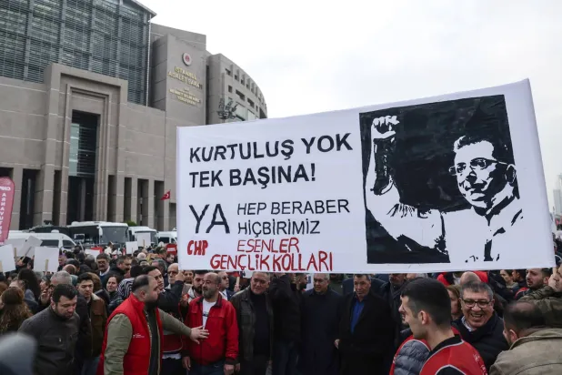 أنصار رئيس بلدية إسطنبول أمام أكرم إمام أوغلو رافعين لافتة كبيرة تحوي صورة له مع عبارات: «لا نجاة لك وحدك... إما أن نكون معا أو لا نكون» خلال إفادته في تحقيقين أمام النيابة الأسبوع قبل الماضي (إ.ب.أ)