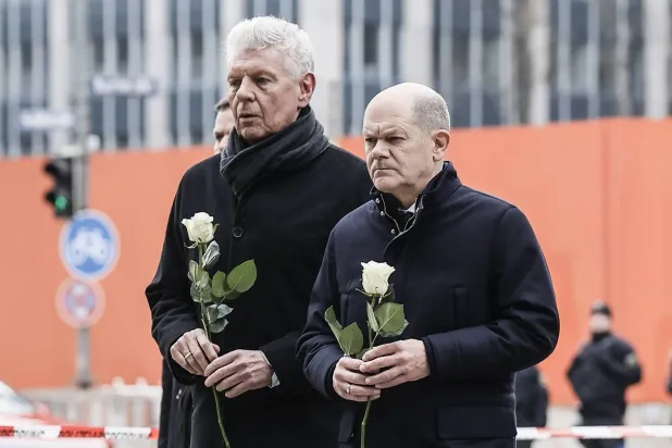 المستشار الألماني أولاف شولتس (يمين) وعمدة ميونيخ ديتر رايتر يحملان وروداً بيضاء خلال زيارة موقع حادث الدهس في ألمانيا (إ.ب.أ)