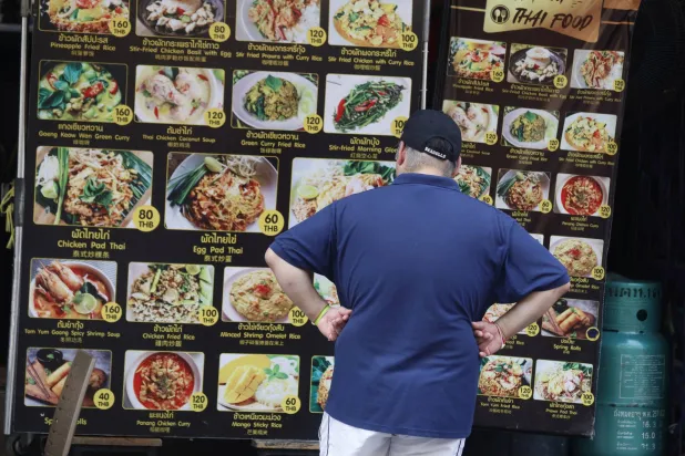 سائح أجنبي ينظر إلى قائمة الطعام التايلاندي داخل أحد المطاعم في بانكوك (إ.ب.أ)