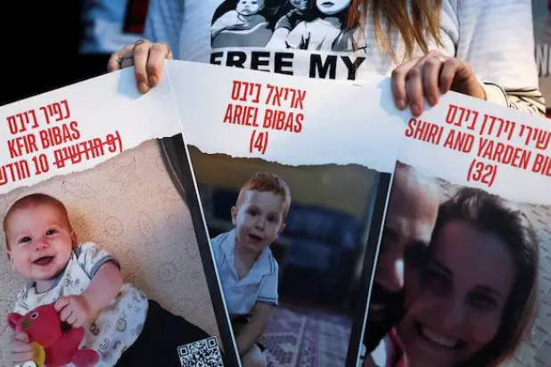 متظاهرة تحمل لافتات تطالب بالإفراج عن الرهائن شيري بيباس وطفليها كفير وأرييل (رويترز)