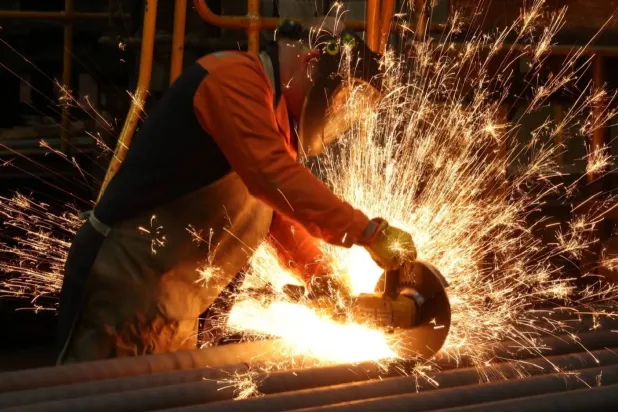 عامل يقطع قضباناً فولاذية مصنَّعة حديثاً في مصنع للصلب ببريطانيا (رويترز)