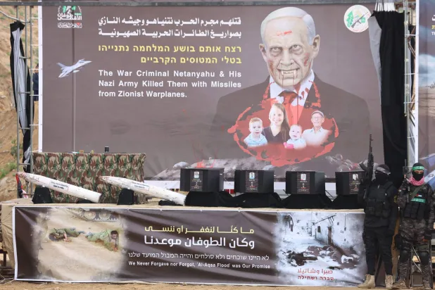 وقف مسلحون فلسطينيون بجانب التوابيت على خشبة المسرح قبل تسليم جثث 4 رهائن إسرائيليين إلى الصليب الأحمر في خان يونس جنوب غزة اليوم (أ.ف.ب)